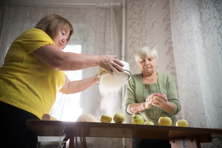 Two old women are making little apple pies. Sifting the flourの写真素材