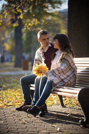 Loving couple sitting and holding a bouquet of autumn leaves in the parkの写真素材