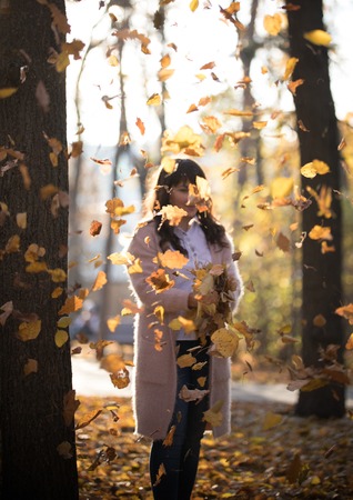 The girl stands under the autumn falling leaves in the parkの写真素材