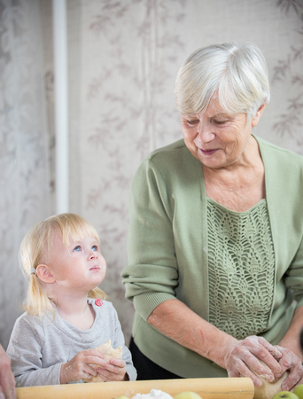 An old woman enjoying making little apple pies with her granddaughter. A little girl smeared with...