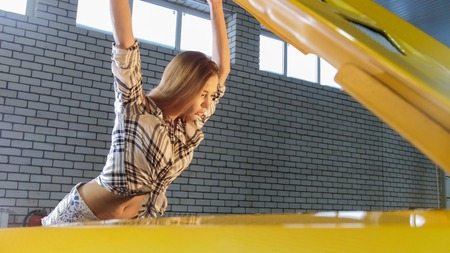 Car repair service. Young sexy woman opens the car hood and looking insideの写真素材