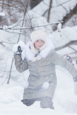Winter forest. A little girl threaten with a snowball. Snowfallの写真素材
