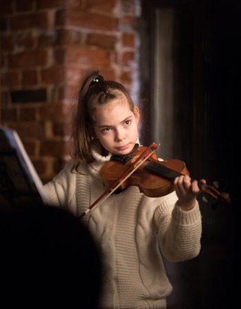 A little beautiful girl in sweater playing violinの写真素材