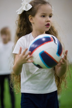 Children playing football indoors. A little girl holding a ballの写真素材