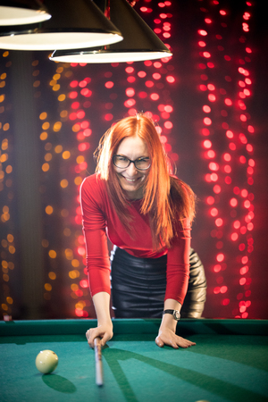 Laughing ginger woman playing billiard holding a cueの写真素材