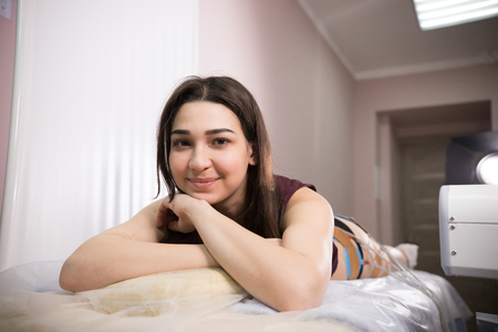 cosmetology beauty clinic. young woman with dark hair taking myostimulation, smiling and looking at the camera at the nutritionists officeの写真素材