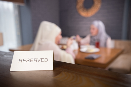 Reserved sign on the table. Two muslim woman sitting on the backgroundの写真素材