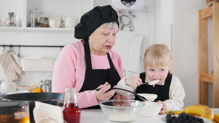 Family making pancakes. An old woman making dough and little girl tasting itの写真素材