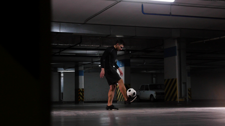 Underground parking lot. A soccer man training his football skills. Balance the ball on his feetの写真素材