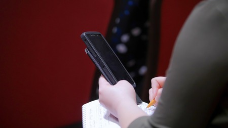 A business conference in the hall. A person sitting on the lecture and making marks in the notebook, holding a smartphoneの写真素材