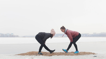 Two slim women standing on the snowy beach and warming up for the runningの写真素材