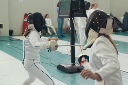 Two young girls fencers having fencing duel on tournament. Mid shot