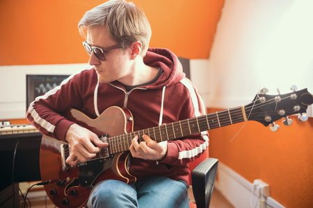 A musician man in glasses playing guitar and recording a song in the studioの写真素材
