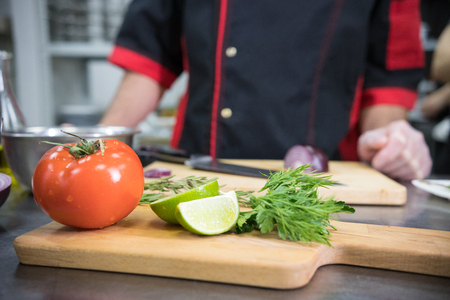 Restaurant kitchen. A tomato and lime on the desk on the foreground. Chef standing on the backgroundの写真素材