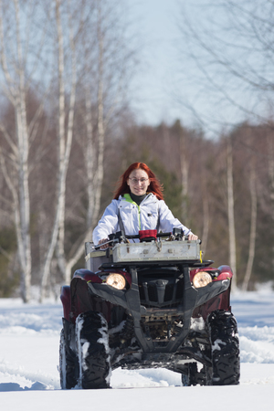 A winter forest. A woman with ginger hair riding big red snowmobile and overcoming the snowの写真素材