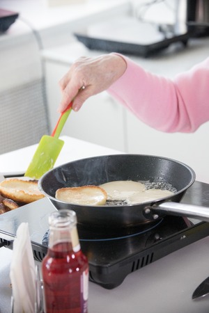 An old woman frying pancakes and turning the pancakes over using a silicone paddleの写真素材