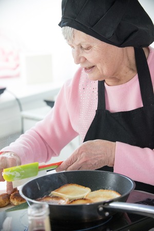 Home kitchen. An old woman making pancakesの写真素材