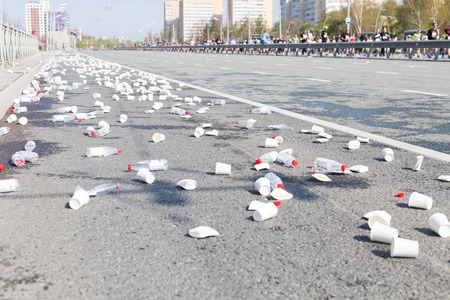 A bunch of plastic cups and empty bottles on the streets while a marathon running