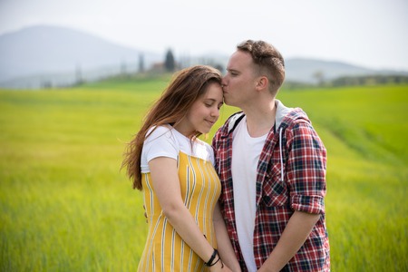 A young happy couple standing on a green meadow. A man kiss his girlfriend in a foreheadの写真素材