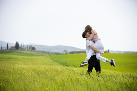 A young happy smiling couple on a green meadow. A man holding his girlfriend on handsの写真素材