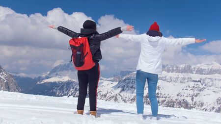 Two young women tourist standing on the hill and looking at the mountains with open arms