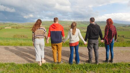 Group of friends standing on the road and looking on the fieldの写真素材