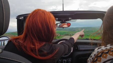 Two women sitting in the cabriolet and riding - a ginger woman pointing at something