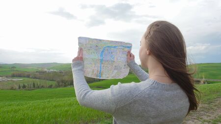 A young woman sits on the green field and looking at the map