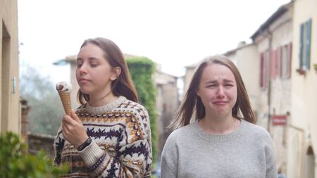 Two young women walking in the town - One of them eat icecream and other is upset