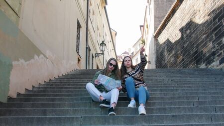 Two young women sit on the stairs and navigate the map of Czech, Prague