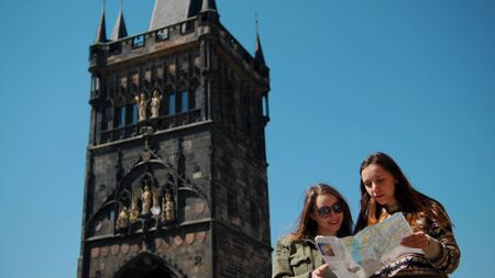 Two young women stand on the background of the old tower and navigate the map