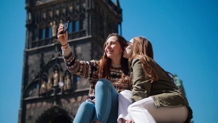 Two young women sit under the old tower and take a selfie with smilingの写真素材