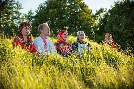 Smiling people in traditional russian clothes sitting on the field in high grassの写真素材