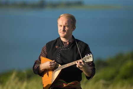 A man in traditional russian clothes playing balalaika on the fieldの写真素材