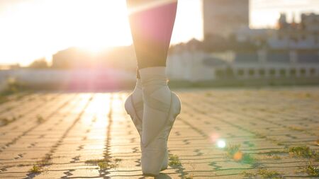 Legs of young woman ballerina standing on the roof on her tiptoes - sunsetの写真素材
