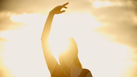 A young woman standing on the roof and raises her hand up - bright sunsetの写真素材