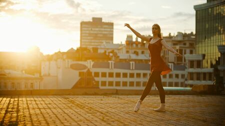 Young graceful woman in red dress ballerina standing in the pose on the roof - bright sunsetの写真素材