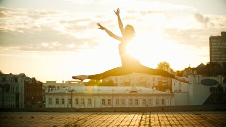 Young woman ballerina jump performing a split on a background of a beautiful bright sunsetの写真素材