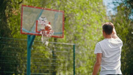 A young man throwing the ball in the basketball hoop and it gets in the target