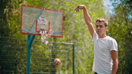 A young man throwing the ball in the basketball hoop and it gets in the target - a man looking in the cameraの写真素材