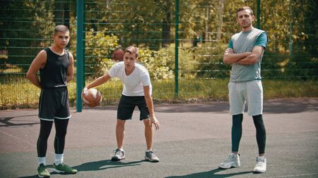 Three sportsmens standing on the basketball court outdoors and looking in the camera - one of them playing with a ballの写真素材