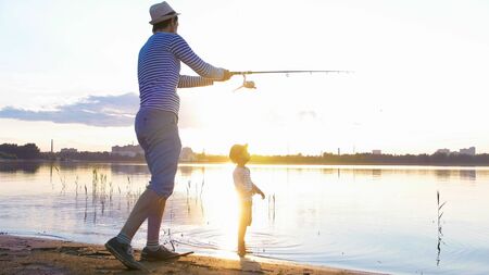 Father and son fishing on the shore of the river at sunsetの写真素材