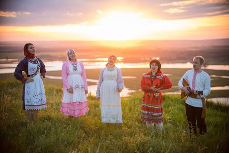People in traditional russian clothes standing on the field on a background on the bright sunset - sing the songの写真素材