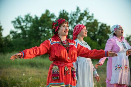 Women in traditional russian clothes standing on the field and looking at the sunsetの写真素材