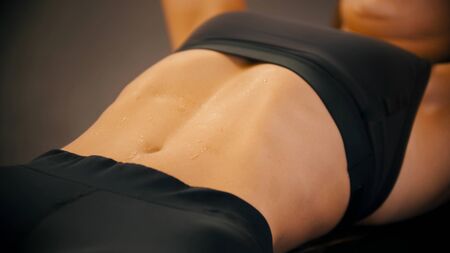 An athlete woman training in the gym - pumping her abs muscles - sweat on the bellyの写真素材