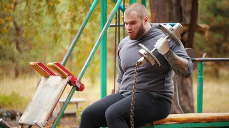 A man bodybuilder pulls up the dumbbells - training on the outdoors sports ground