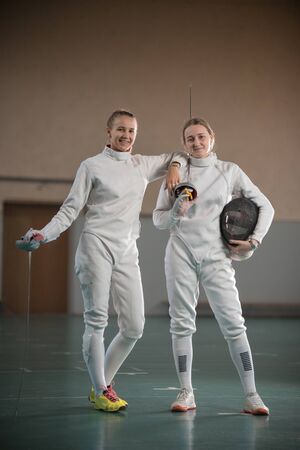Two young women fencers looking at the camera and holding swordsの写真素材