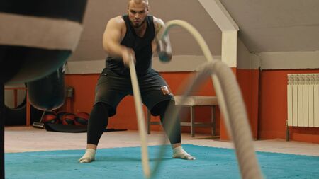 Big powerlifter actively waves the ropes by his hands