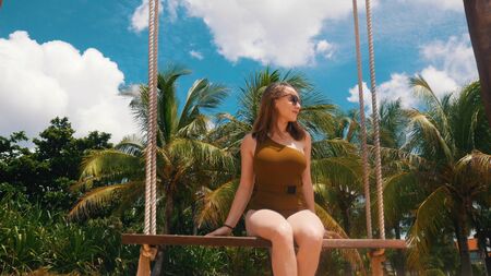 Beautiful girl is riding on a swing on the beach with palm trees - outdoorの写真素材
