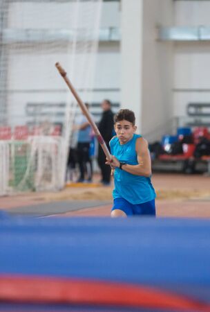 Pole vaulting indoors - guy in a blue shirt running holding a poleの写真素材